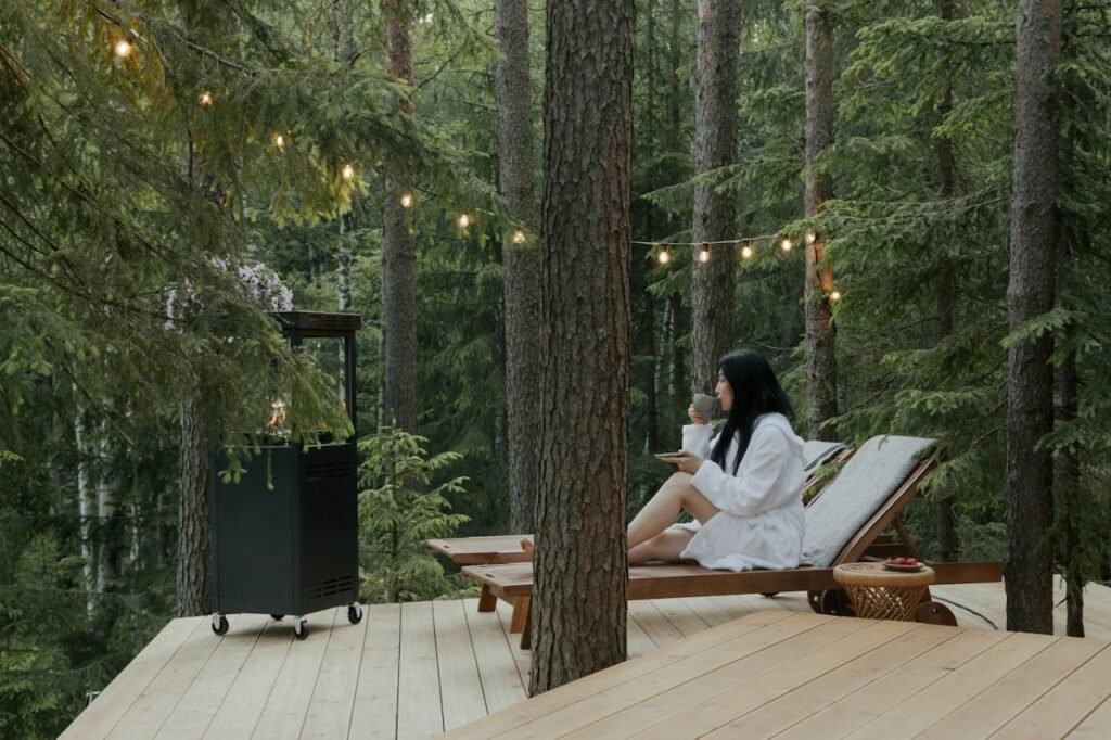 tea lounge Woman in bathrobe relaxing on a deck with drink, surrounded by forest tranquility.
